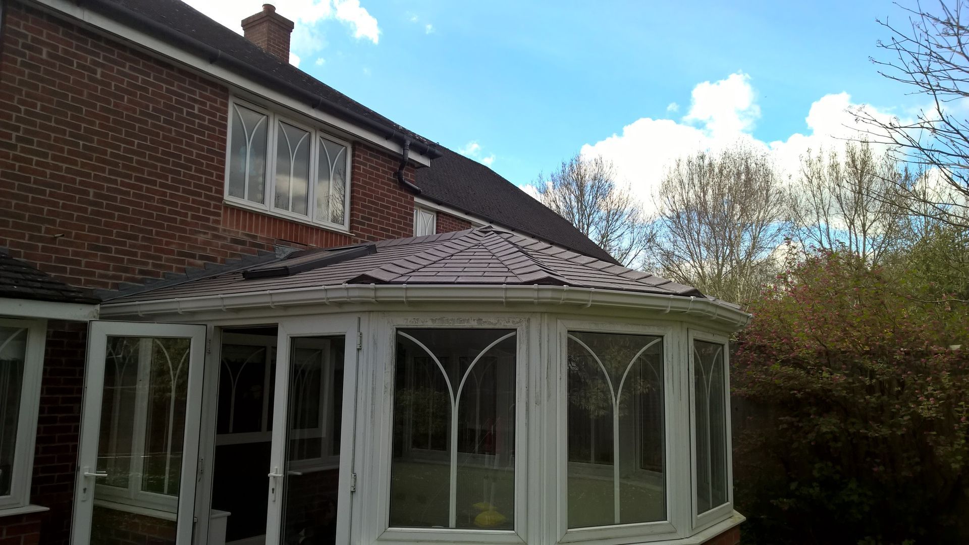 A white conservatory with a tiled roof is next to a brick house.