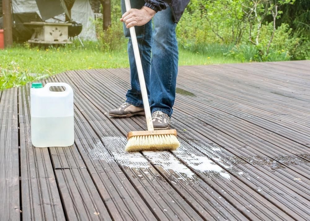 A man is cleaning a wooden deck with a broom.