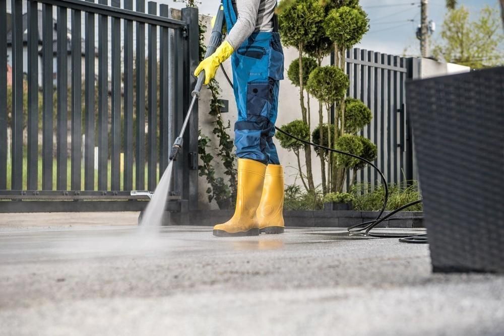 A man is using a high pressure washer to clean a driveway.