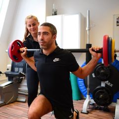Sporty young man doing squats exercises with assistance of his sports therapist in Rehab Pro Sports Injuries and Wellness clinic. Coaching assistance training concept