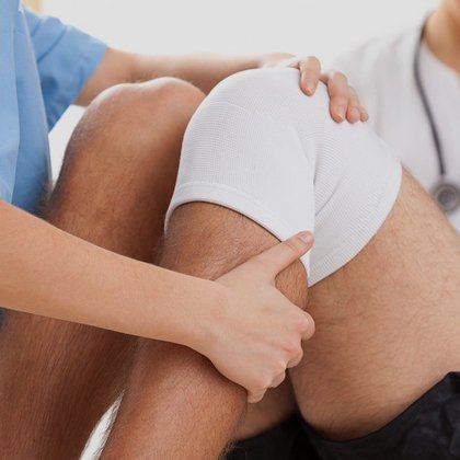 A man with a bandage on his knee, being examined by a therapist
