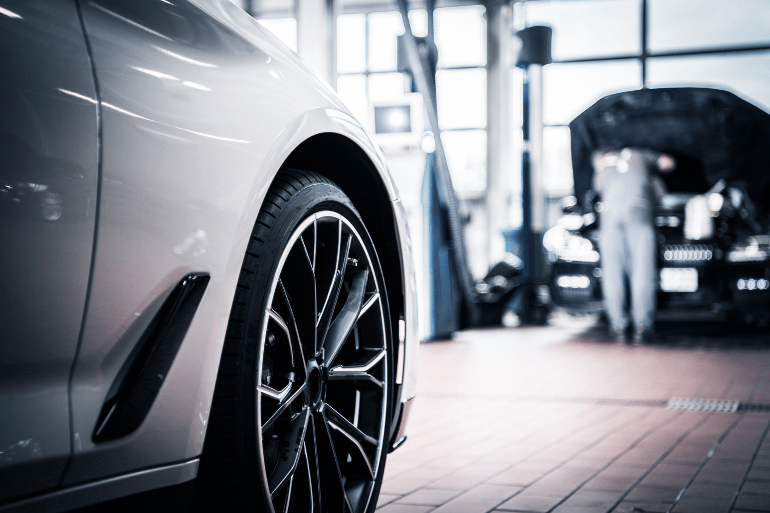 Silver car wheel in auto shop, mechanic working on another vehicle in the background.