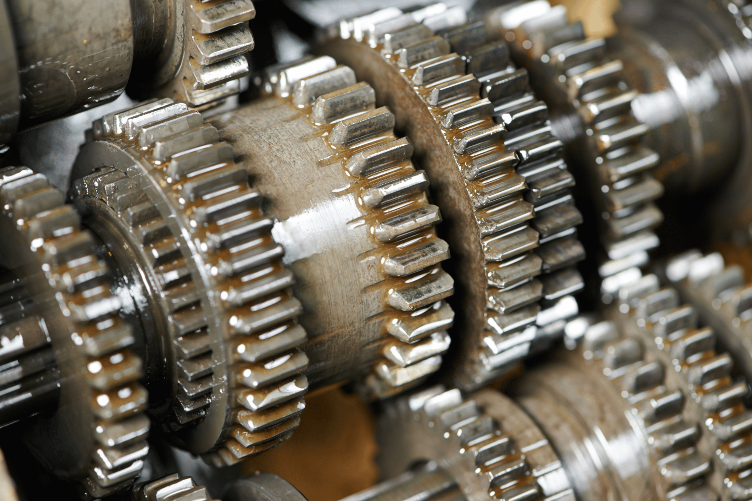 Close-up of metal gears meshing together, coated in oil.