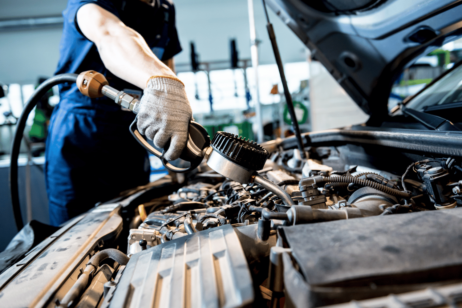 Mechanic in blue uniform working on a car engine with a tool, in a garage.