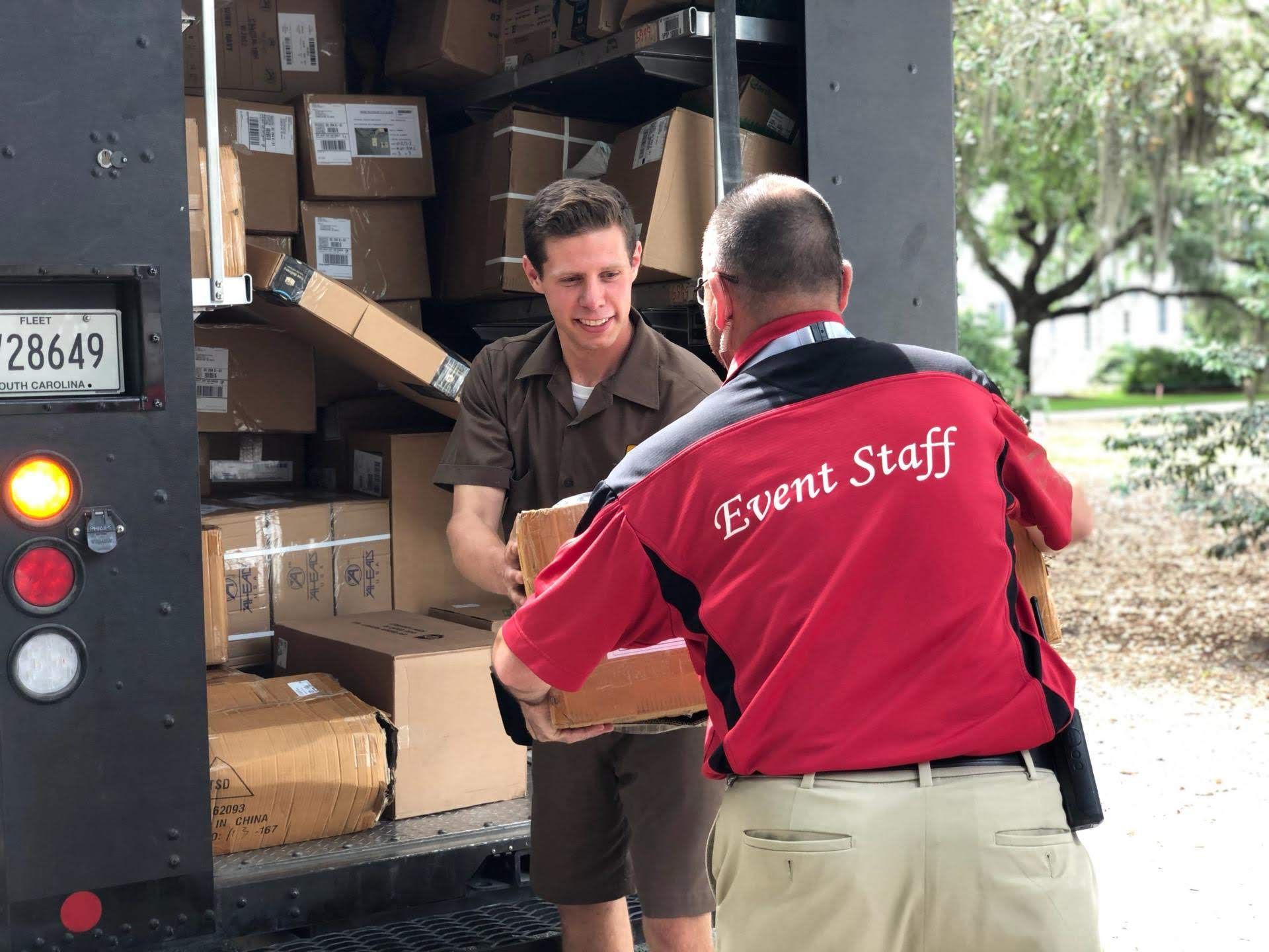 A man wearing a red shirt that says event staff is loading boxes into a truck.