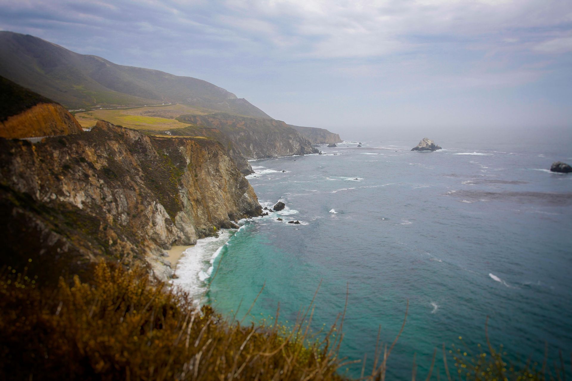 A view of the ocean from a cliff with mountains in the background.