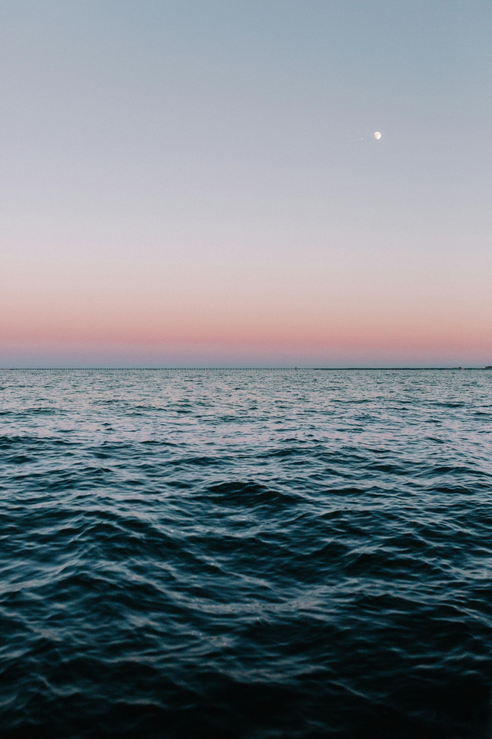 There is a full moon in the sky over the ocean.