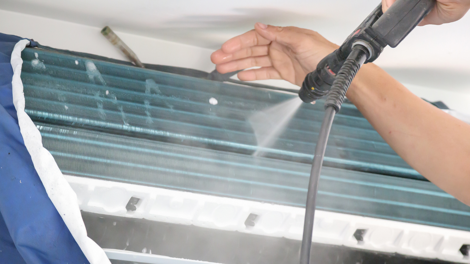 A person is cleaning an air conditioner with a high pressure washer.