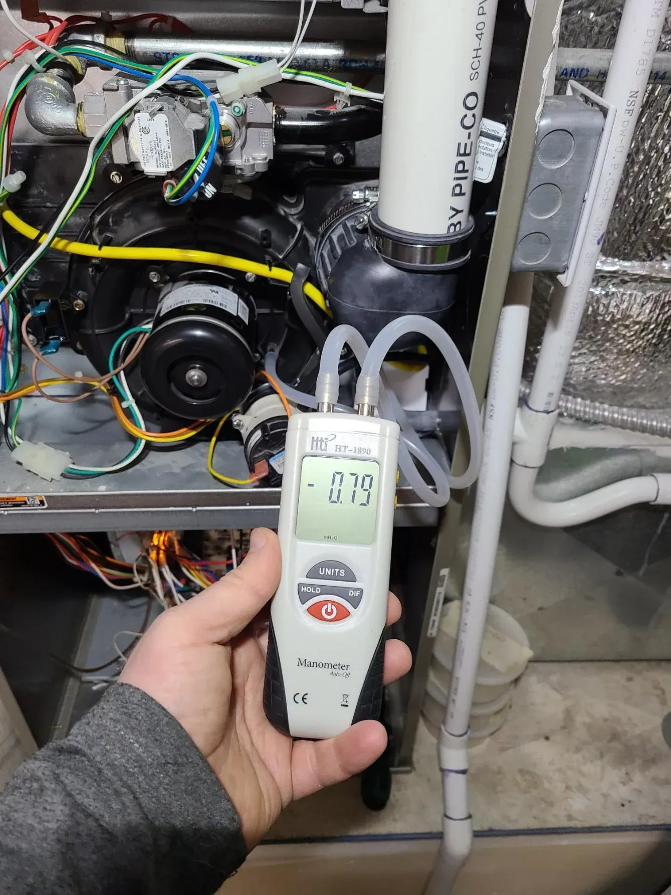 A person is holding a pressure gauge in front of a heater.