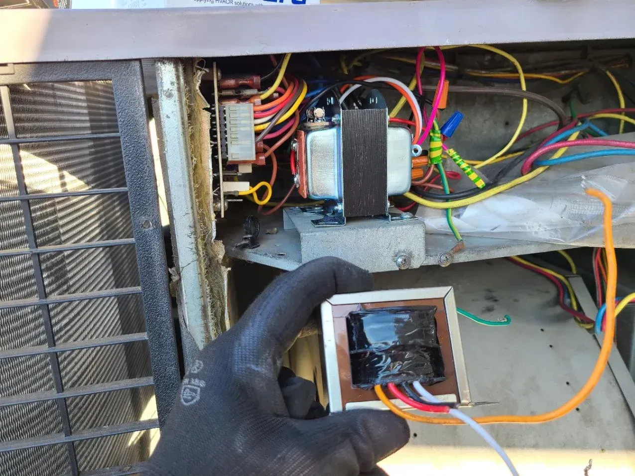 A person is holding a transformer in their hand in front of an air conditioner.