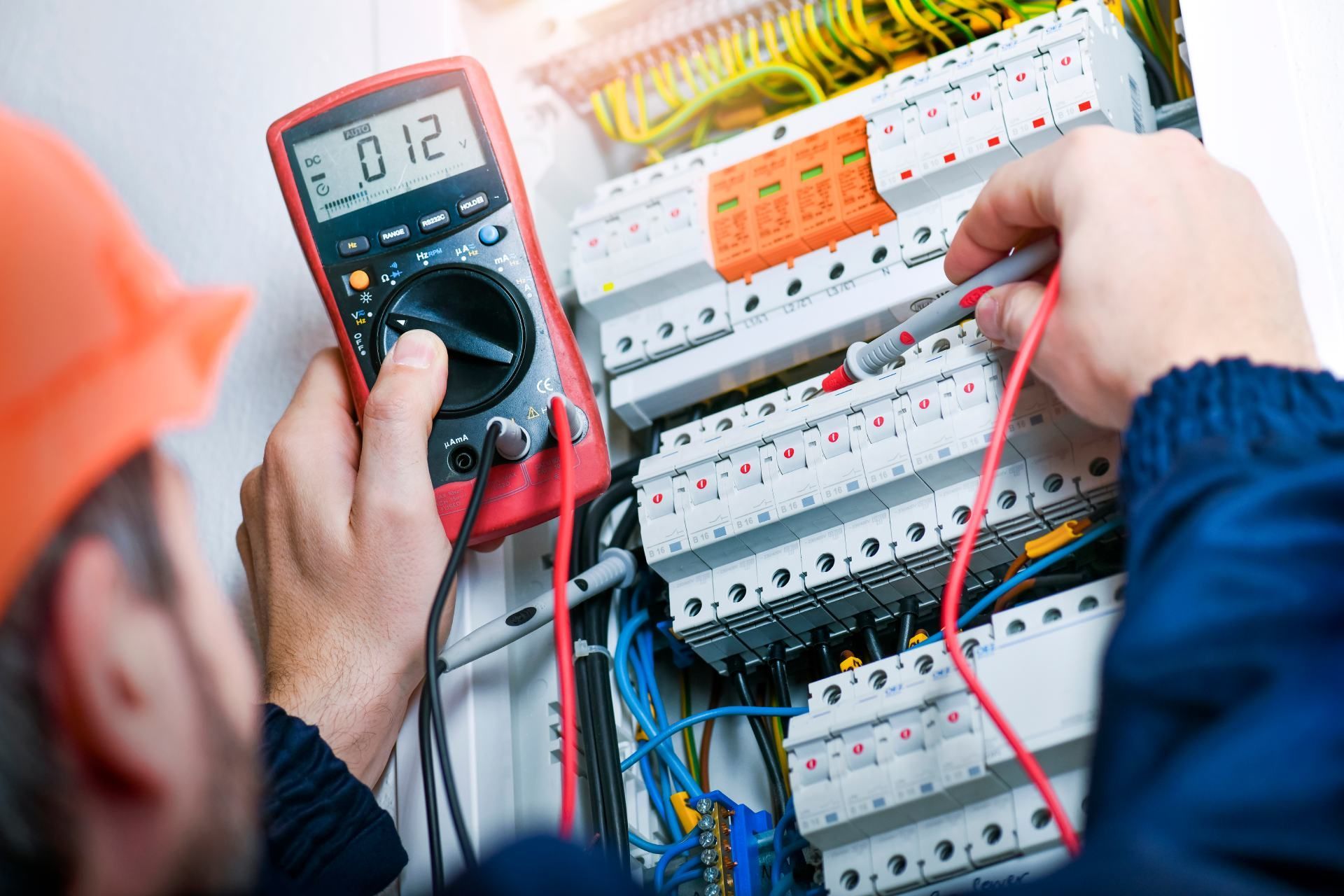 Electrician using a multimeter to test wiring in a circuit breaker panel.
