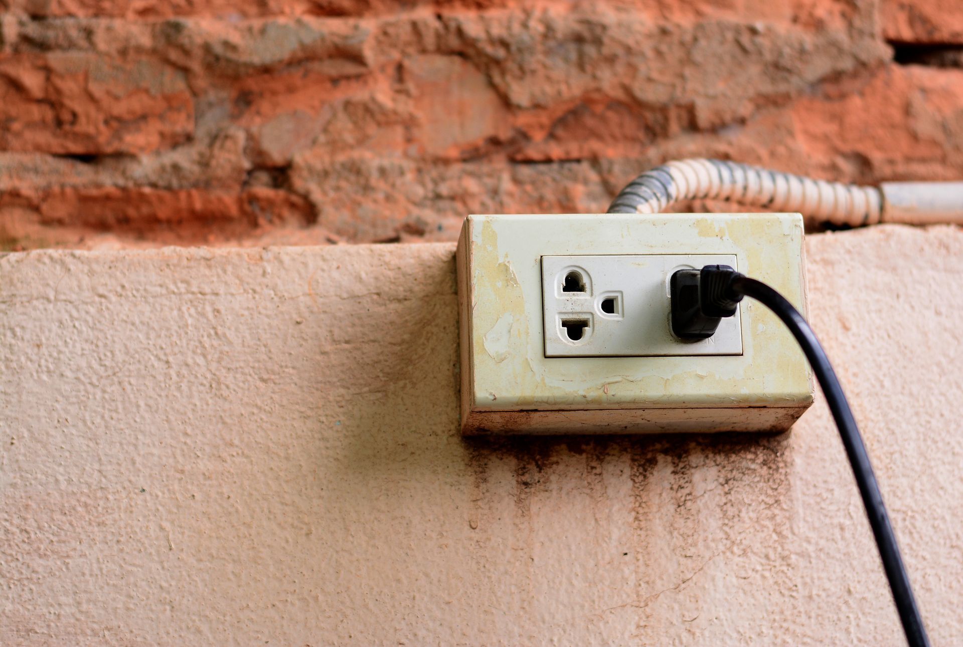 Electrical outlet with plug in an old, weathered wall.