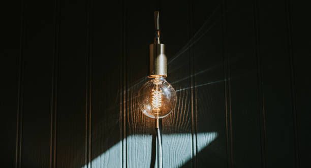 Lit bulb hanging from a gold fixture against a dark green wall. Shadow cast below.
