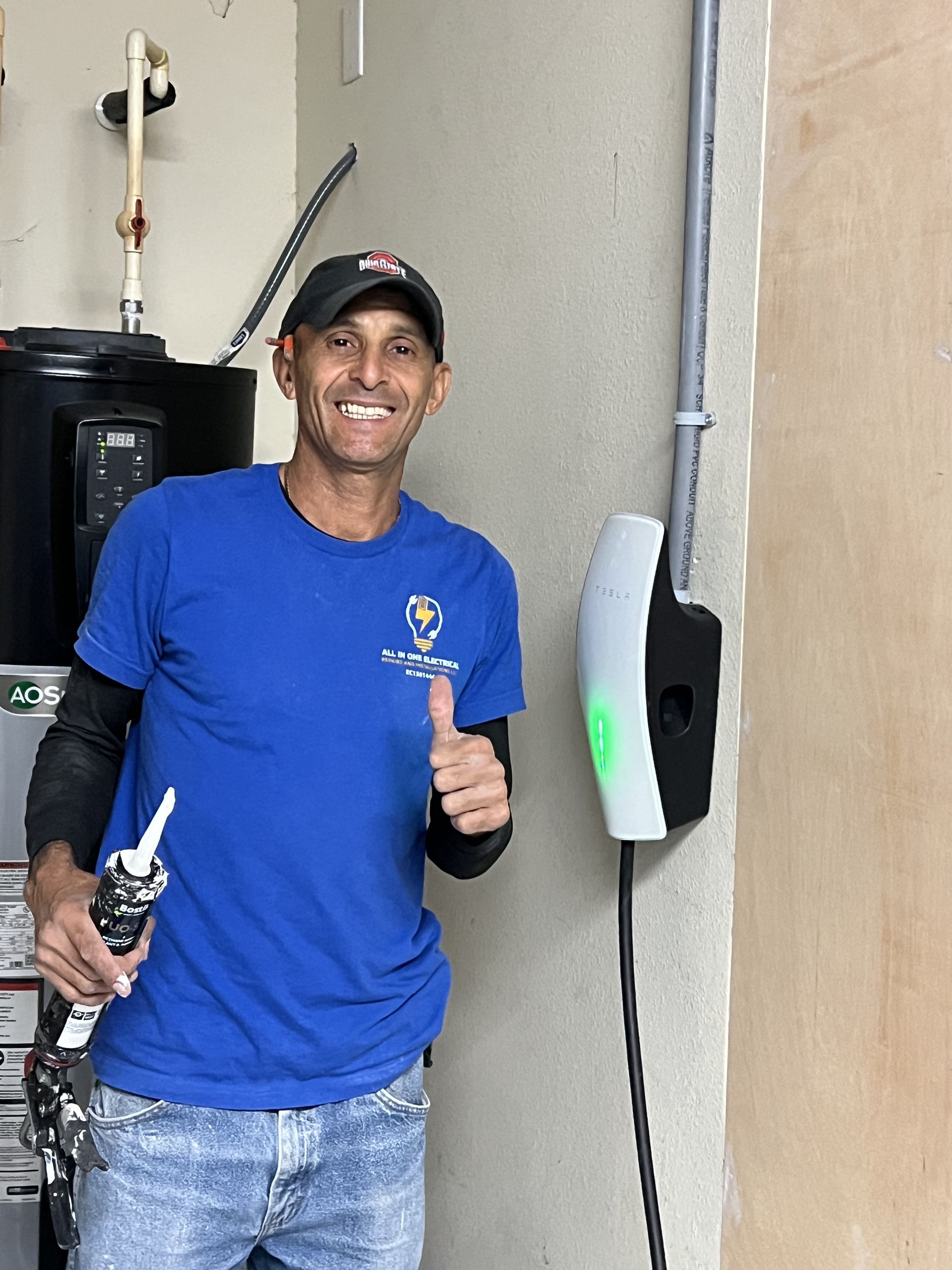 Man in blue shirt gives thumbs up next to an electric vehicle charger in a garage.