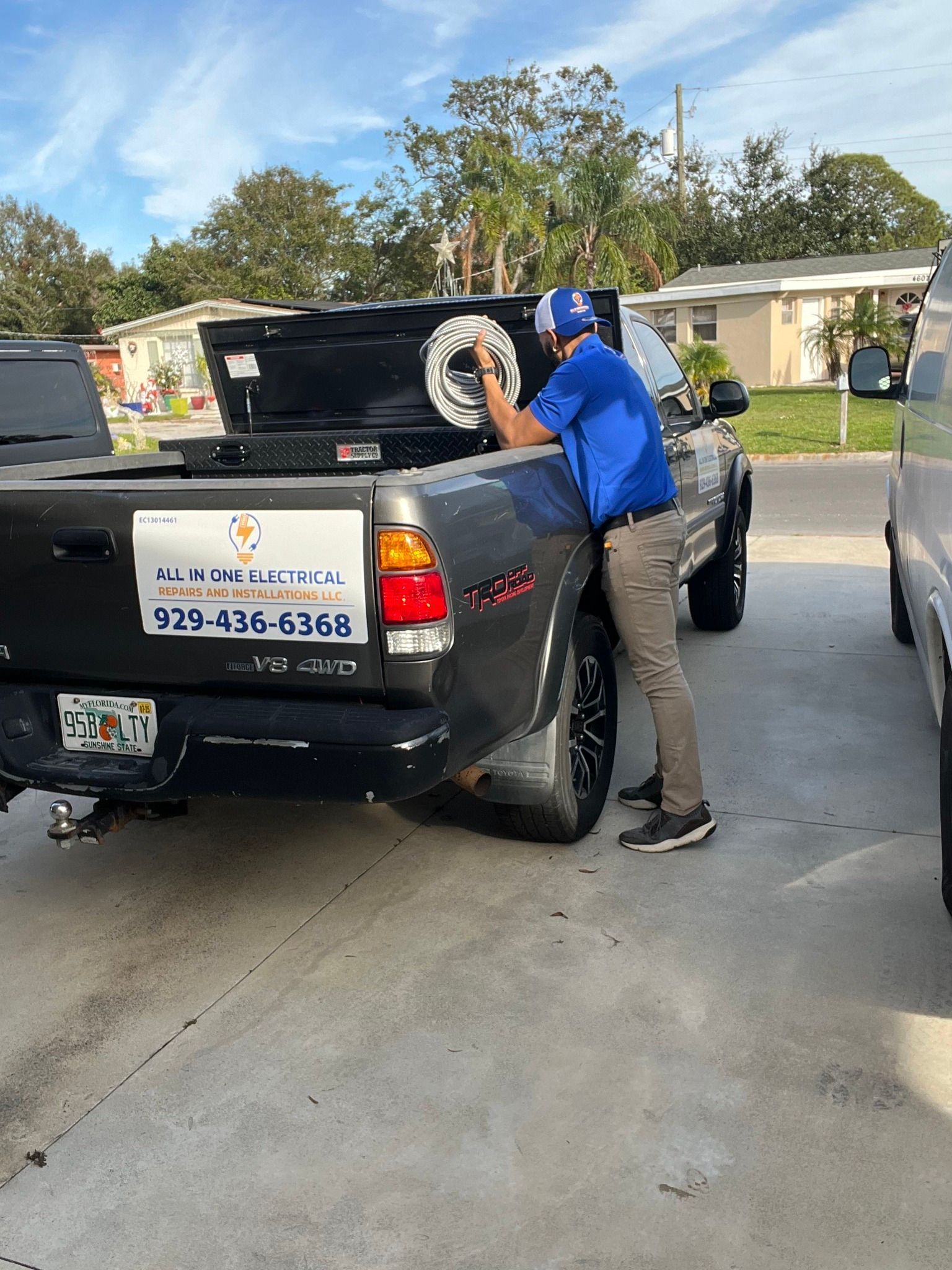 Man in blue shirt working on a black pickup truck in a driveway. Truck has company logo.