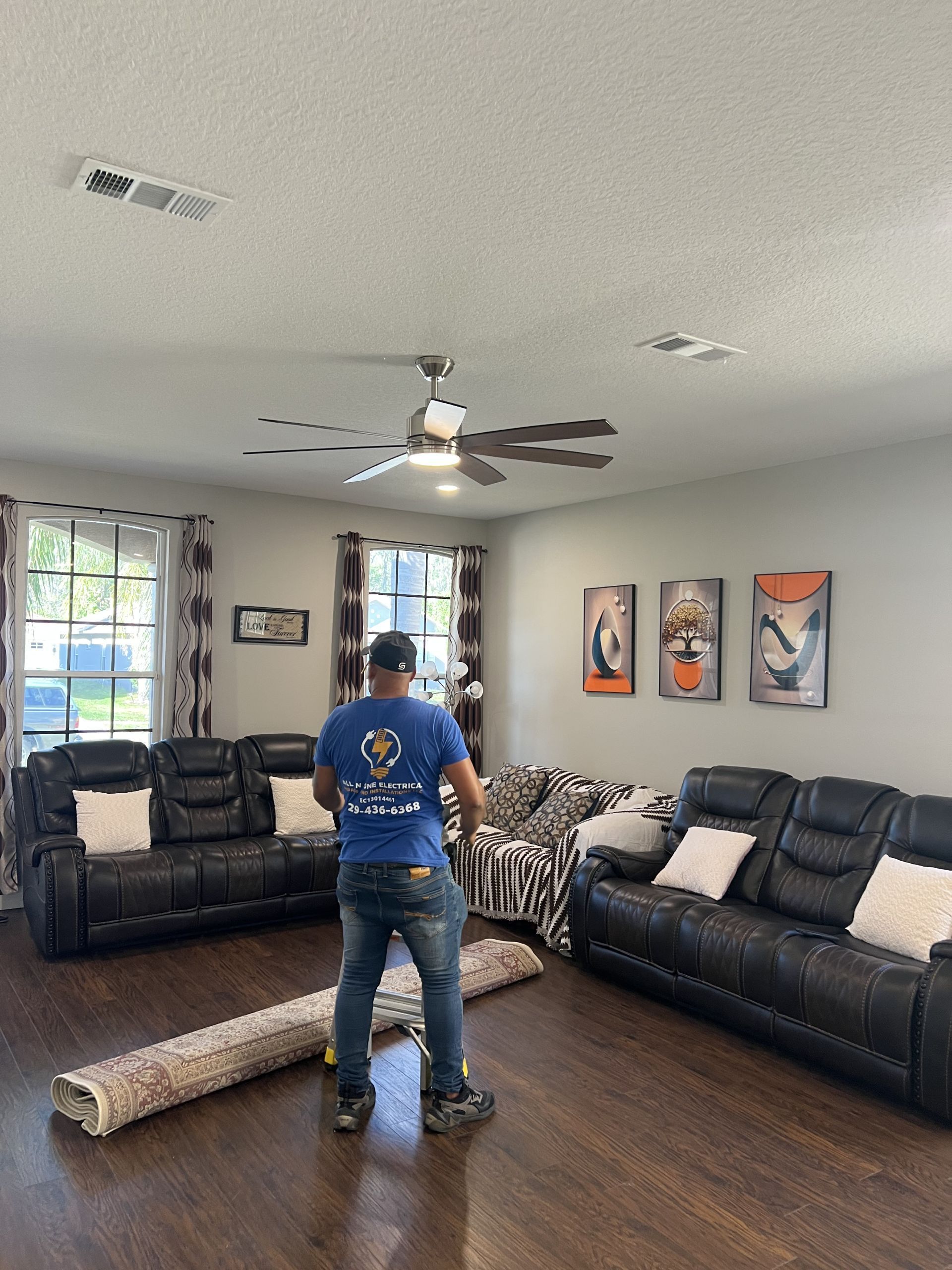 Man rolling out rug in living room with black leather sofas and art.