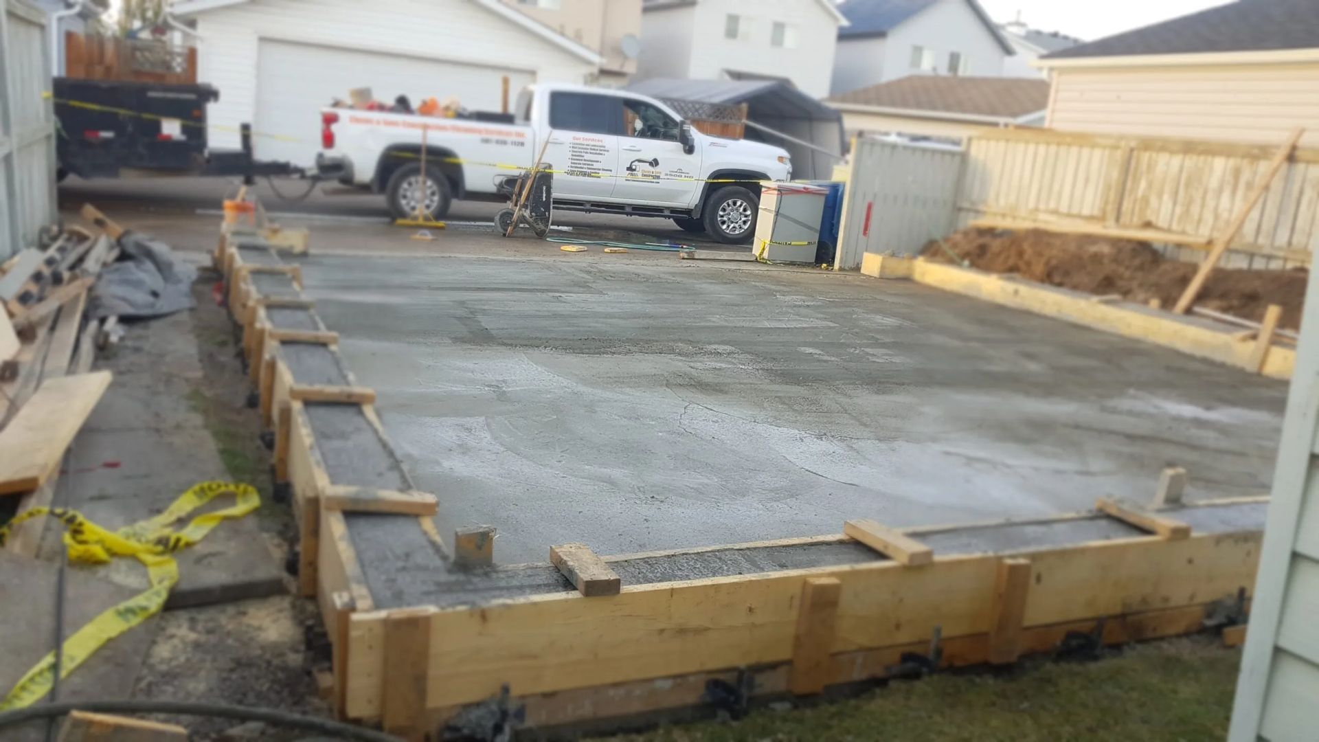 A fresh concrete slab poured inside wooden forms for a new construction project in a residential backyard.