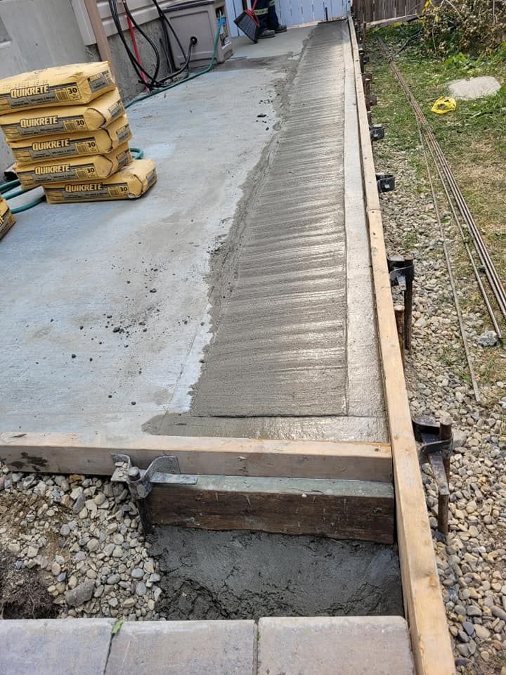 Freshly poured concrete strip alongside a wooden frame in a residential yard.