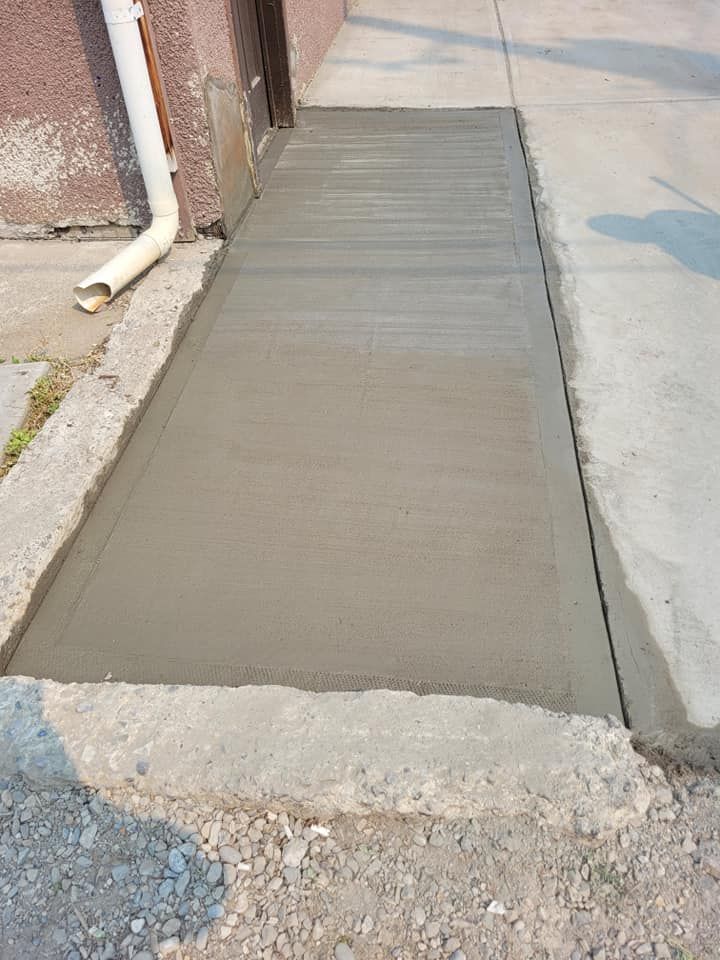 A freshly poured concrete ramp between two existing sidewalks next to a building wall.