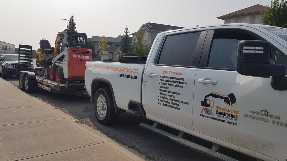 A white pickup truck with company branding on the side pulling a trailer carrying a Bobcat skid-steer loader.