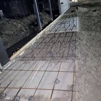 A construction site shows a concrete slab with metal wire mesh reinforcement installed in preparation for a new pour.