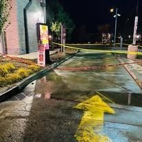 A paved drive-thru lane at night, cordoned off by yellow caution tape, featuring a large yellow arrow painted on the ground.