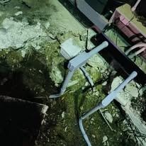 Two gray, L-shaped electrical conduits emerge from a dark, rough concrete floor near the edge of a dark structure.