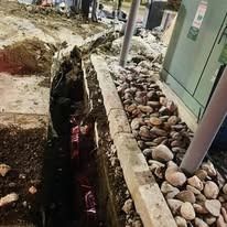 A construction site with a deep narrow trench next to a concrete curb lined with decorative river rocks.