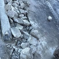 A pile of broken gray concrete chunks lies next to a paved surface.