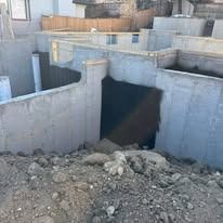 Concrete foundation walls for a building under construction, viewed from an excavated dirt lot.