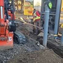 A construction worker in a high-visibility vest stands in a trench next to an excavator at a McDonald's drive-thru.