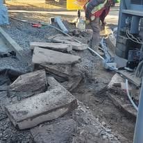 A worker in a high-visibility vest inspects electrical conduits emerging from the dirt at a construction site.