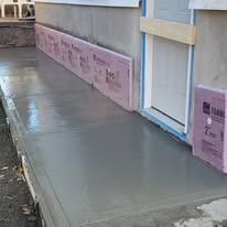 Freshly poured concrete walkway against a foundation wall with pink foam insulation boards.