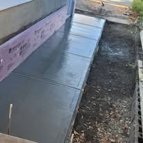 A freshly poured concrete sidewalk runs alongside a building foundation insulated with pink rigid foam boards.