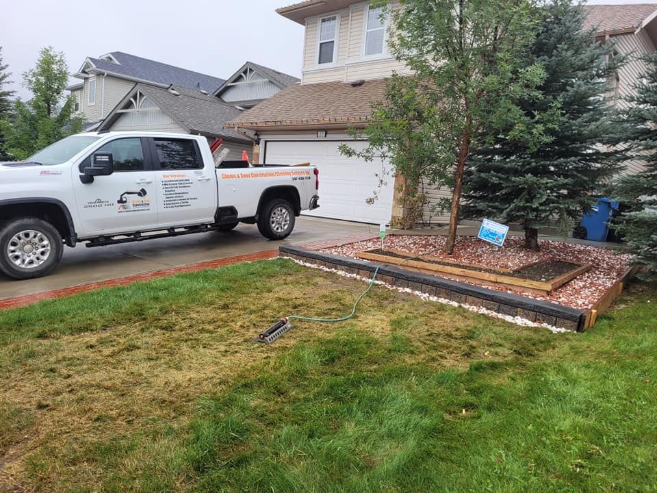 A white pickup truck parked on a suburban driveway next to a landscaped garden bed with a small tree and red mulch.