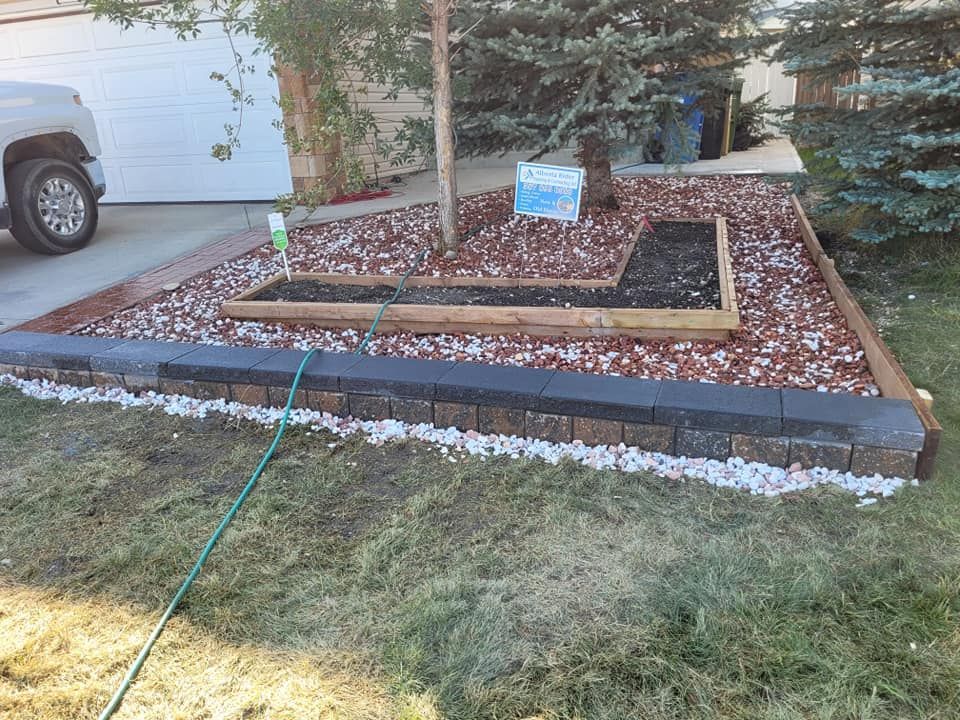 A landscaped front yard featuring a stone retaining wall, an L-shaped wooden planter box, reddish mulch, and a large tree.