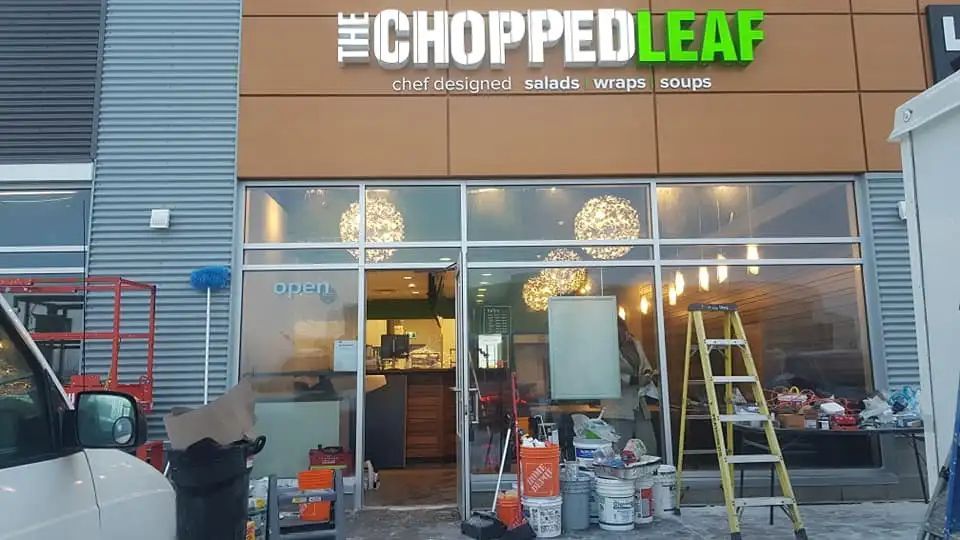A storefront for The Chopped Leaf, featuring a tan facade with green and white signage and construction gear outside.