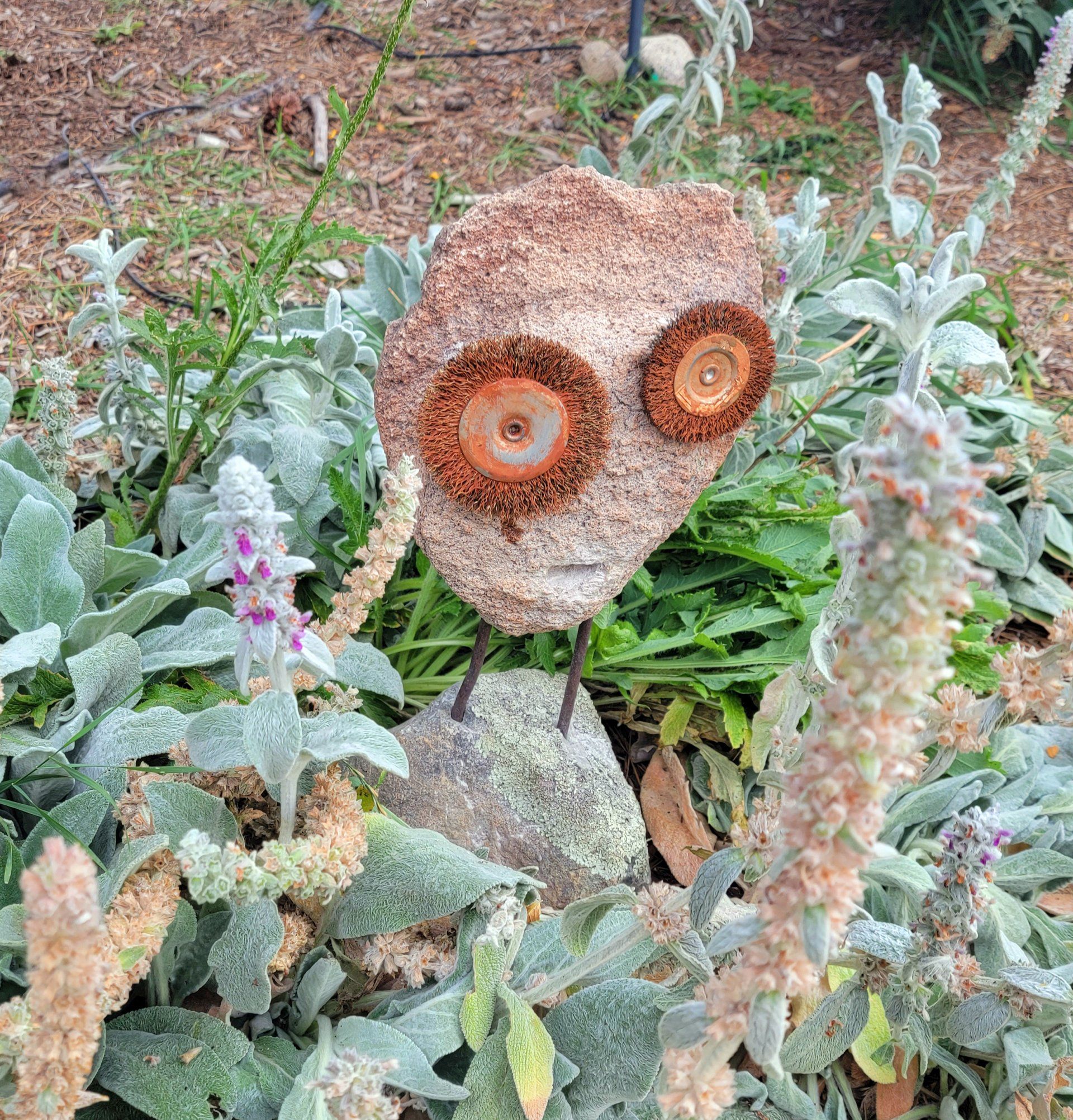 A rock with a face on it is sitting in the middle of a garden.