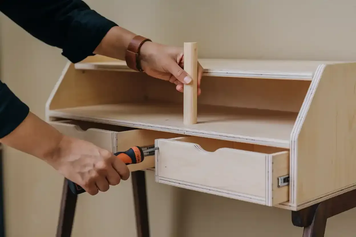 A person is working on a wooden desk with a screwdriver.
