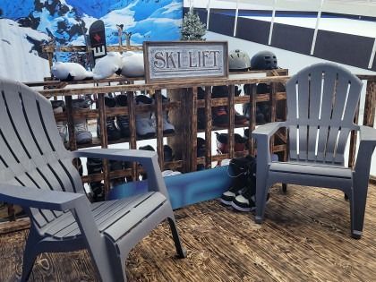 Two gray Adirondack chairs sit in front of a wooden rack holding ski equipment, and a 