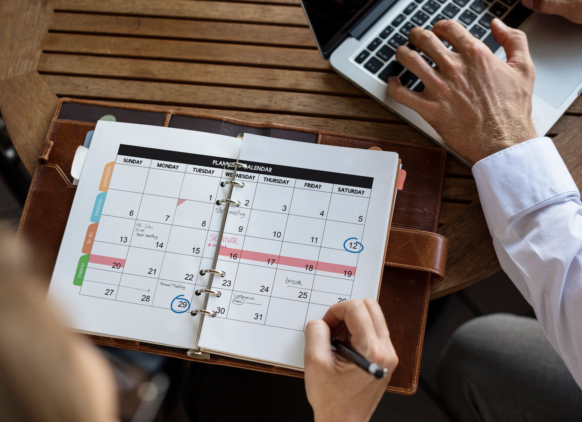 A person is sitting at a table with a calendar and a laptop.