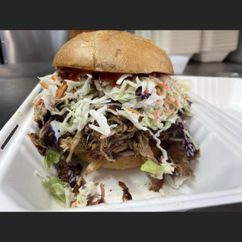 Pulled pork sandwich with coleslaw in a white container. The sandwich sits on a tan bun, with pulled pork topped with creamy coleslaw.
