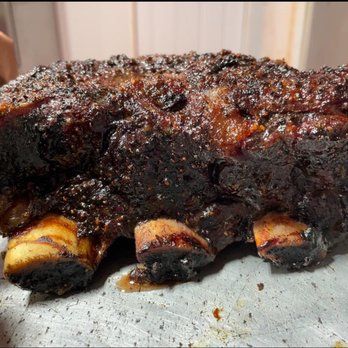 Smoked beef short ribs with a dark, crusty exterior and visible bones on a metal tray.