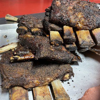 Smoked beef short ribs stacked on a metal tray, with a dark, charred exterior.