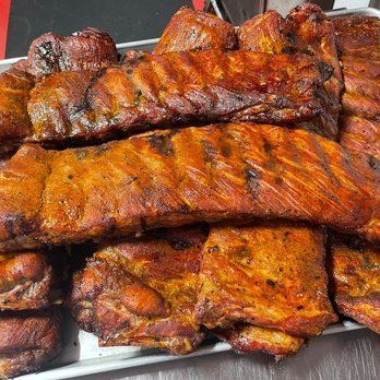 Close-up of a tray of smoked ribs with a reddish-brown color, piled together and ready to eat.