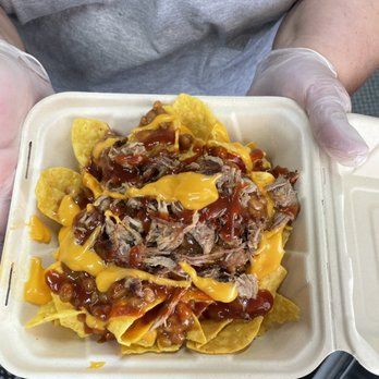 Pulled pork nachos with cheese sauce and BBQ sauce, served in a takeout container.