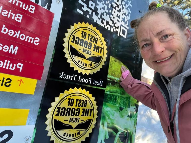 Woman smiling next to a food truck sign, pointing to a 