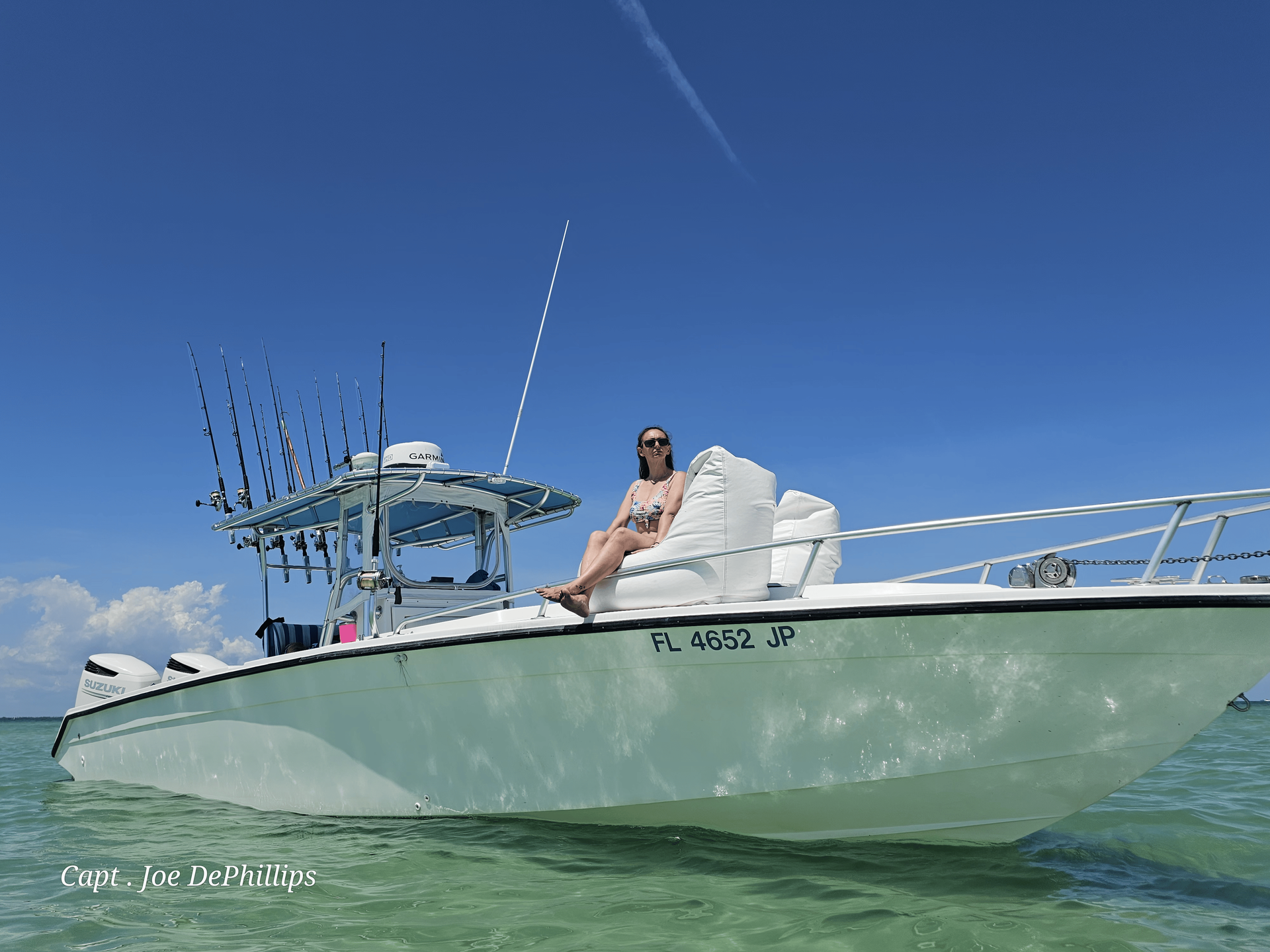 Woman sitting on white boat in clear turquoise water under a blue sky.