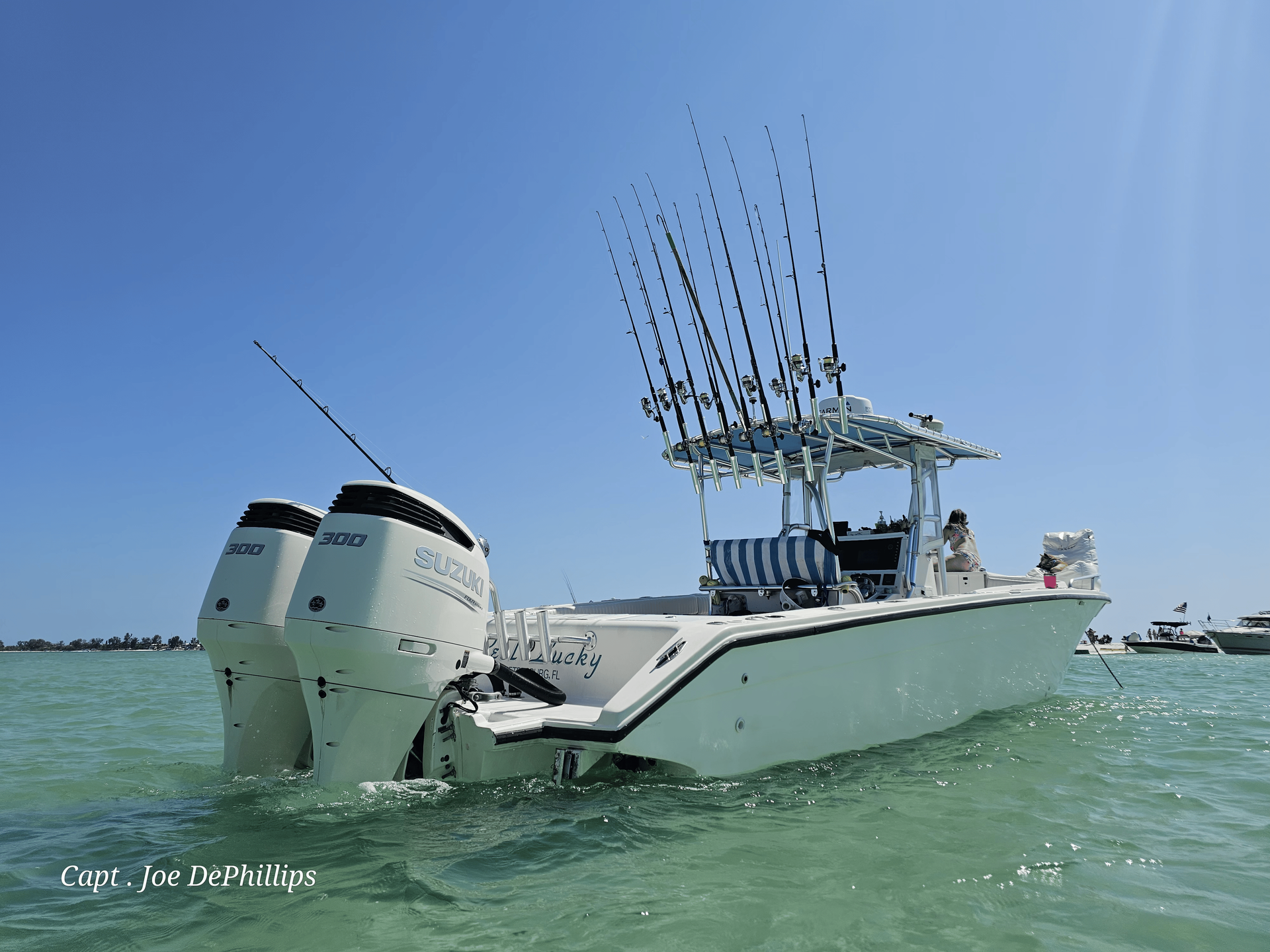 White fishing boat in clear water with two motors, many fishing rods, and a blue sky.