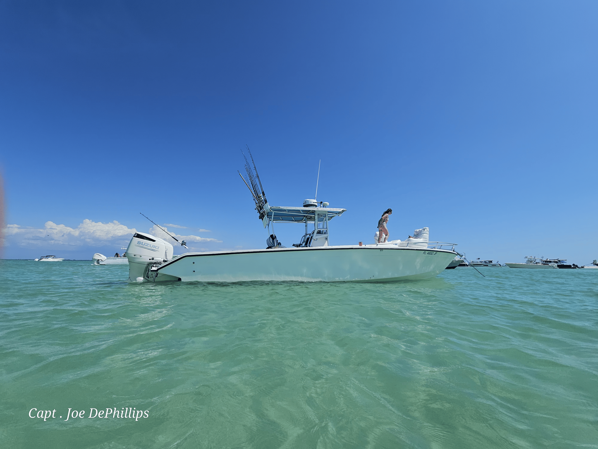 White boat in clear turquoise water under a bright blue sky; people aboard.